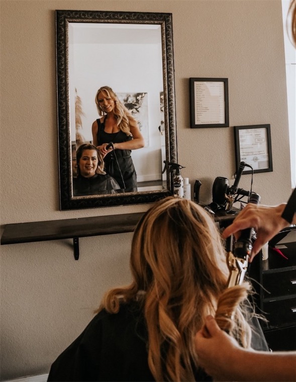 Stylist styling a client's hair in front of the mirror