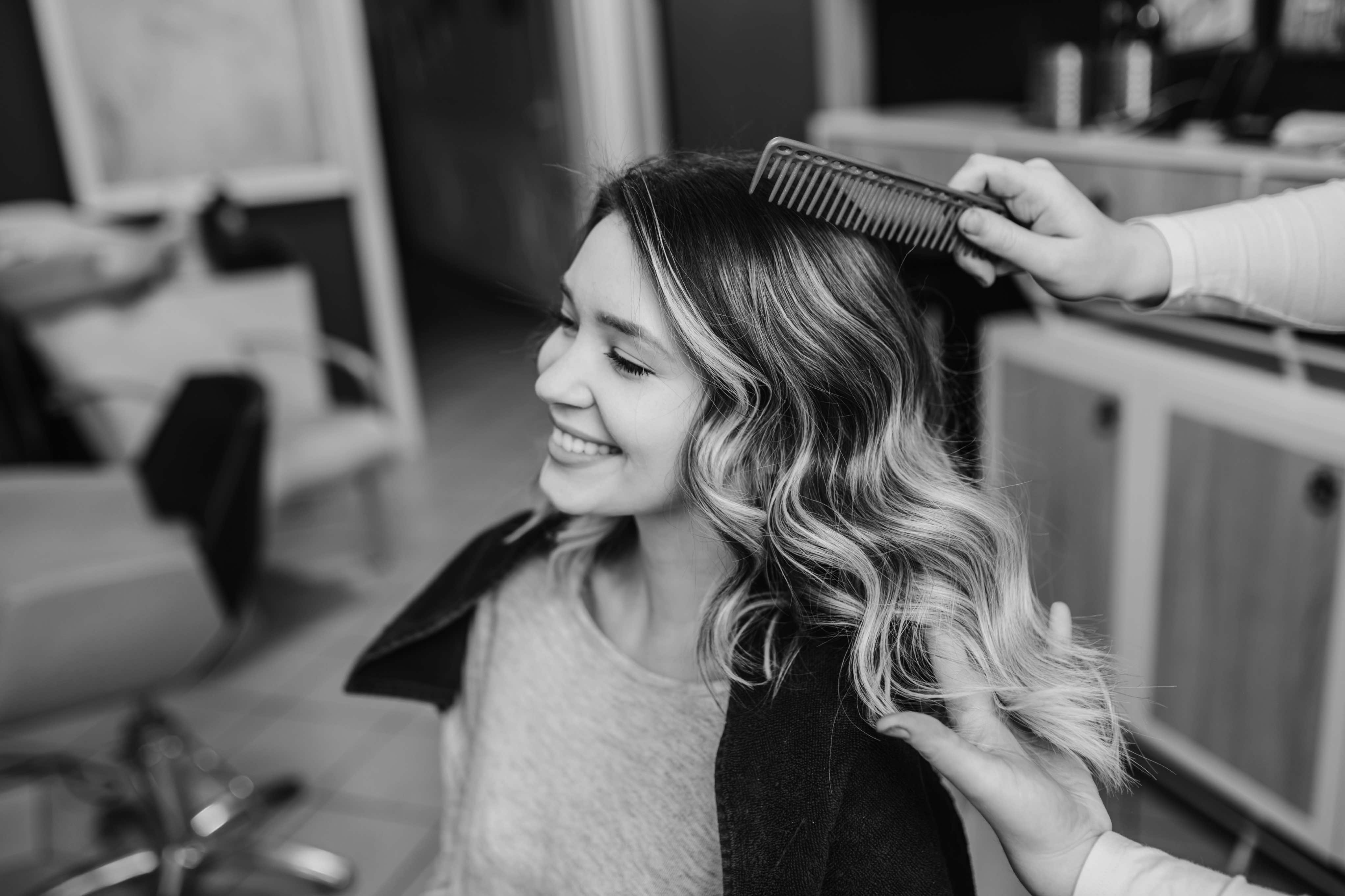 Stylist brushing out soft balayage waves for a smiling client