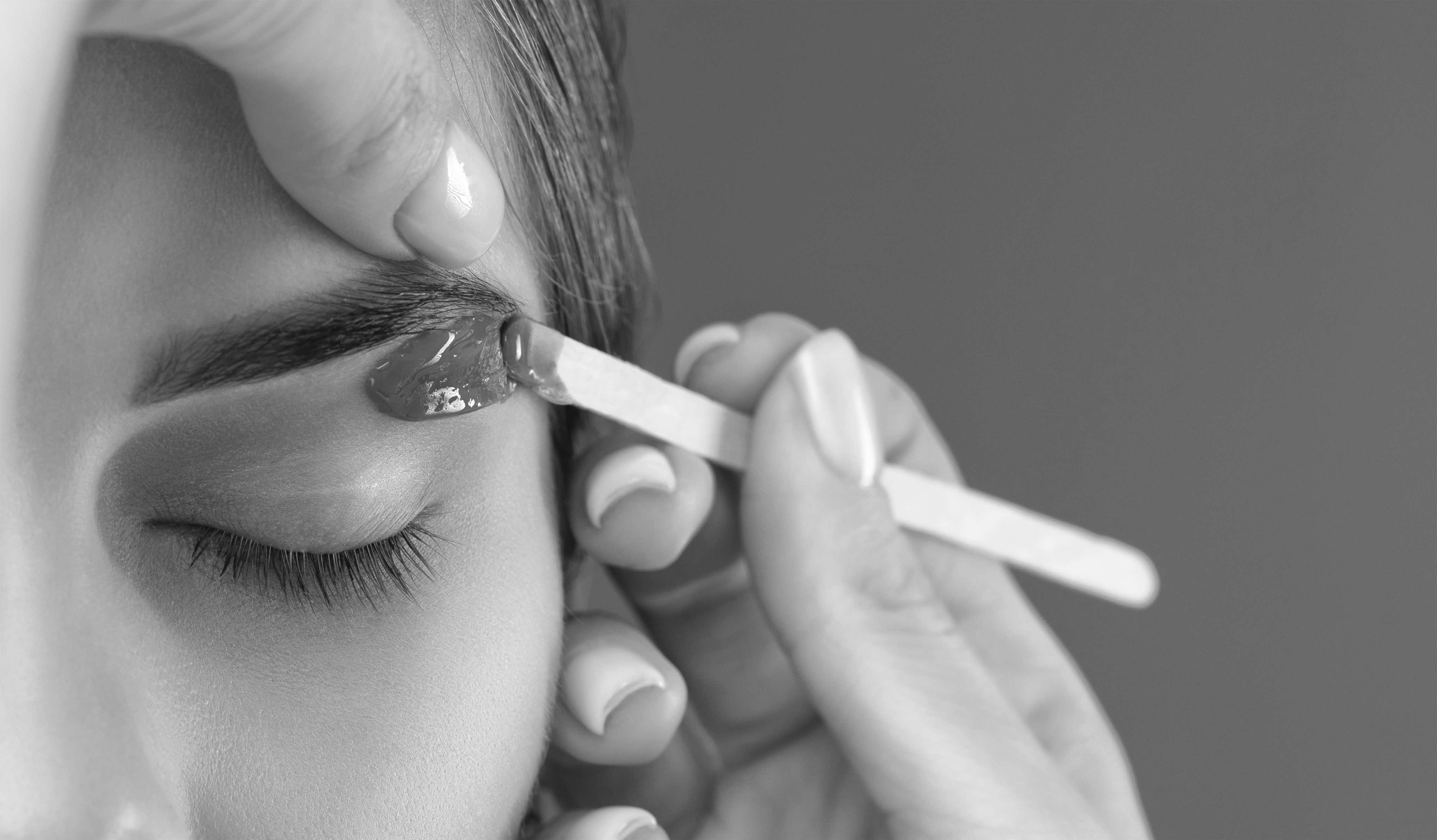Esthetician shaping an eyebrow with warm wax