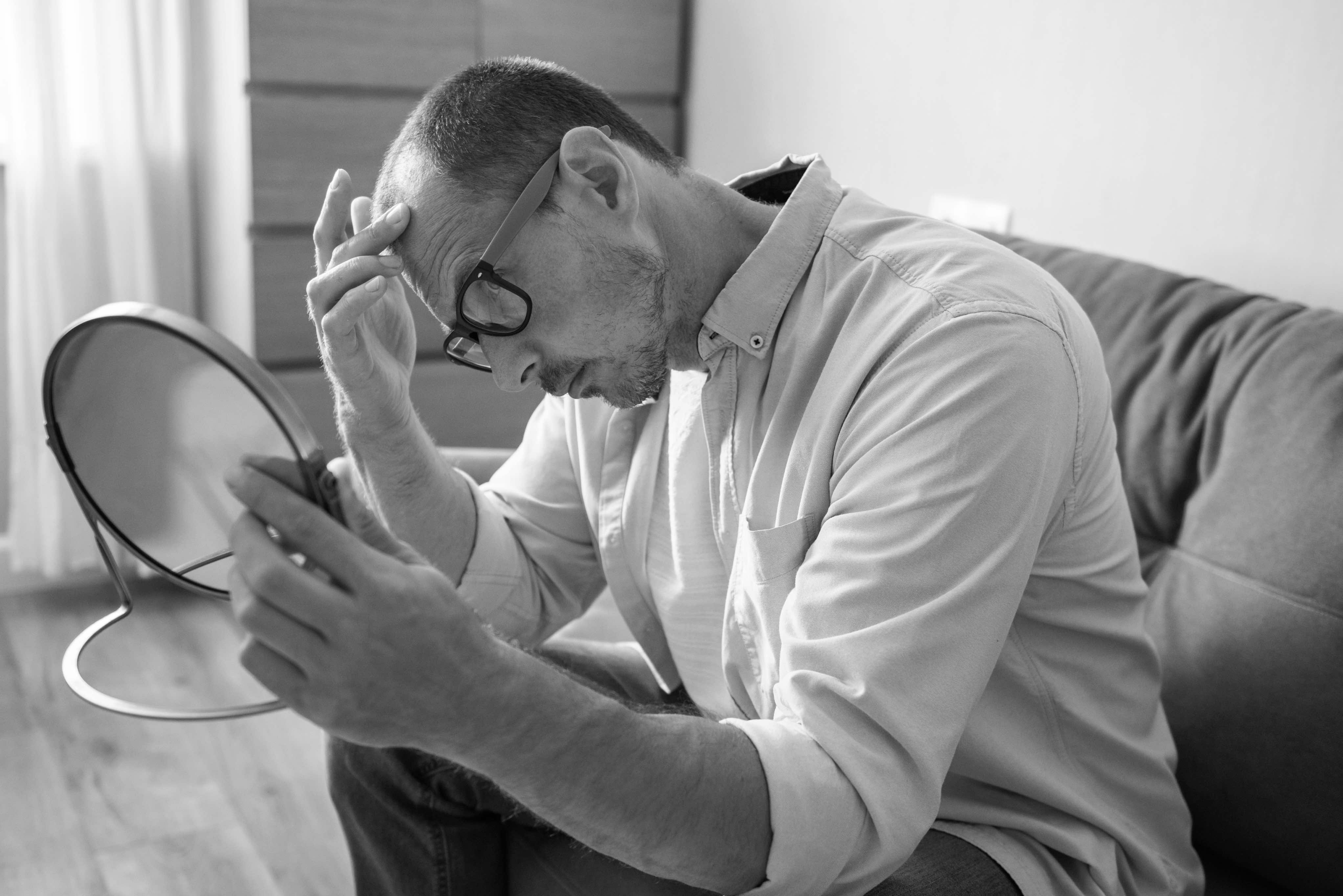 Man checking thinning hair in a hand mirror